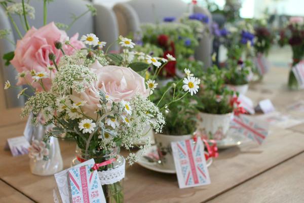Event flowers Birmingham: Vintage china teacups filled with summer flowers and labelled with floral union jacks are displayed on a wooden table.