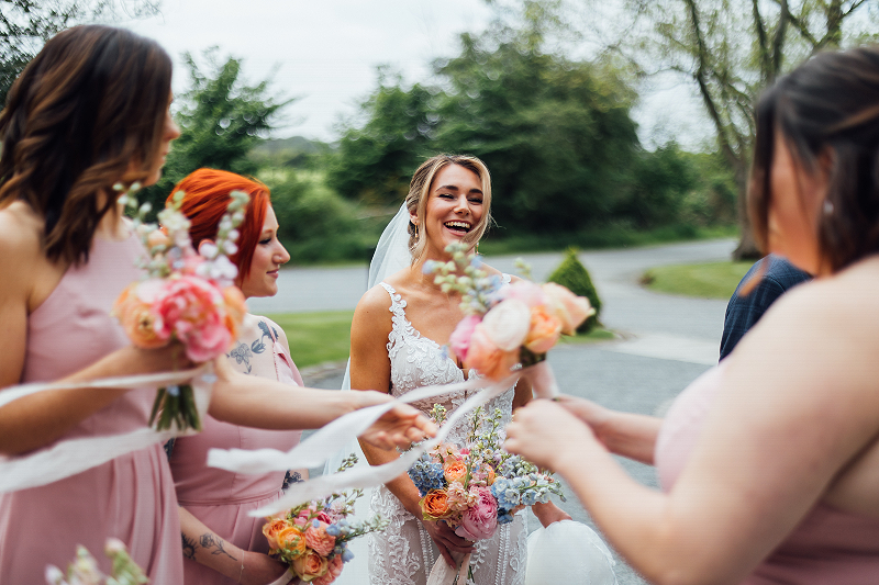 A bride laughs with her bridesmaid as they hold their wedding flower bouquets outside Shustoke Barns, Warwickshire.