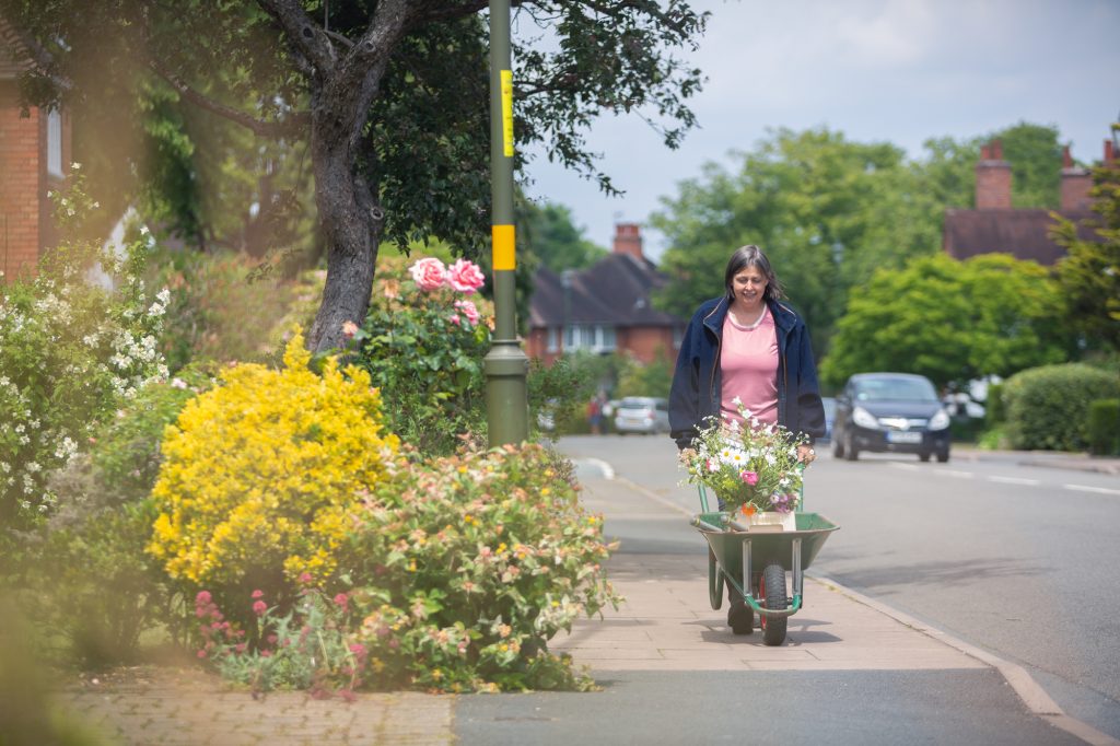 Flower grower and florist Carole of Tuckshop Flowers pushes a wheelbarrow full of her locally grown flowers through the leafy streets of Bournville on her way home from her local allotment. Contact Carole to discuss flowers.