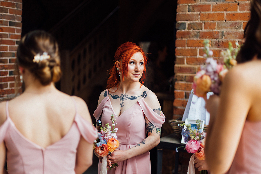 A spring bridesmaid holds bridesmaid bouquet with coral ranunculus and blue delphiniums at this Shustoke Barn wedding, Warwickshire.
