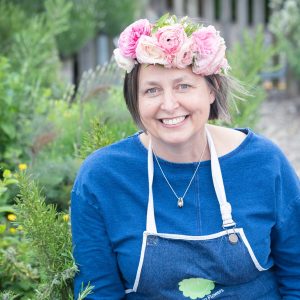 Event florist, wedding florist and funeral florist Carole of Tuckshop Flowers wears a spring flower crown and smiles at the camera.